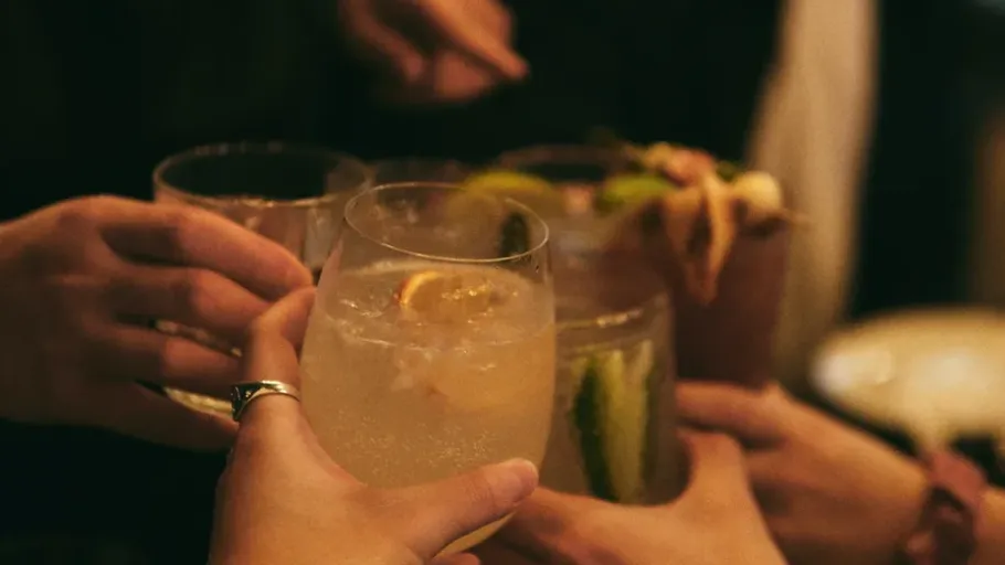 Hands clinking glasses in a dimly lit setting.