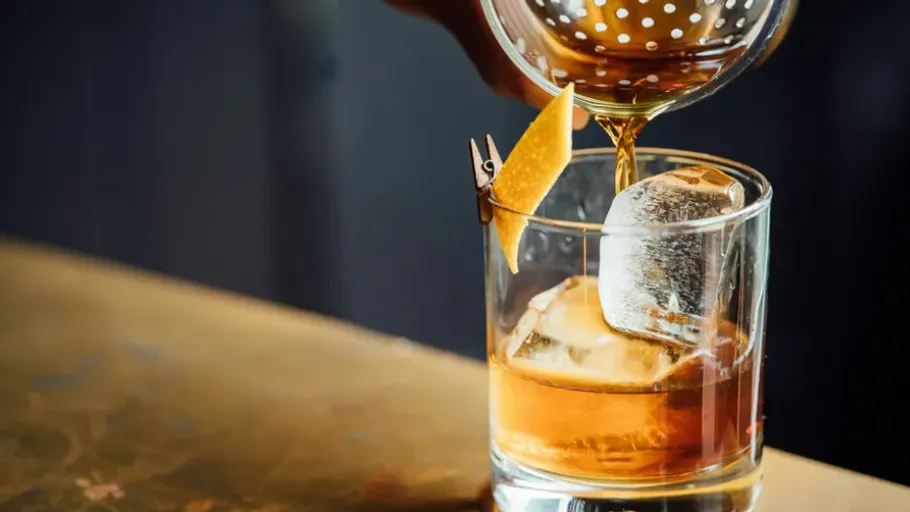 Whiskey being poured over ice with garnish.