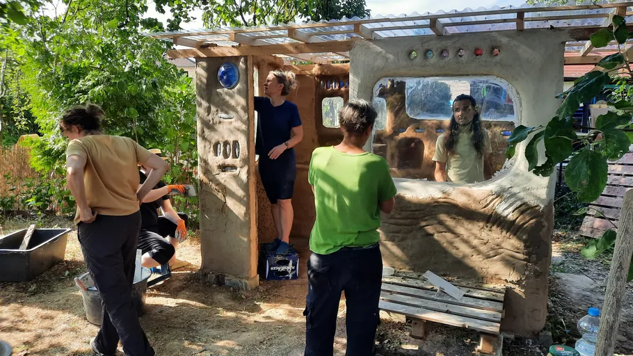 People building a structure with clay in garden.