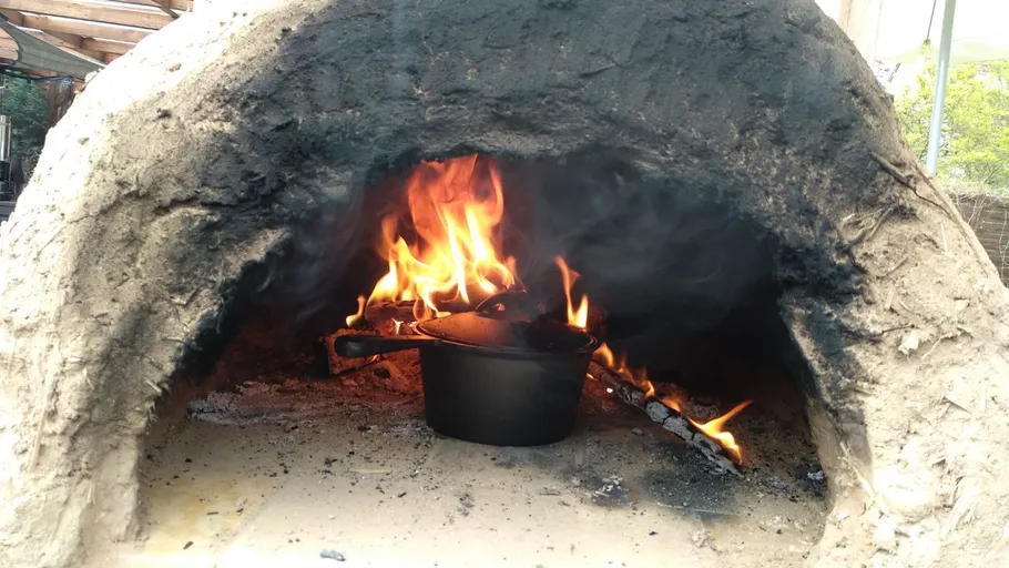 Lehmofen mit Feuer und Topf innen.