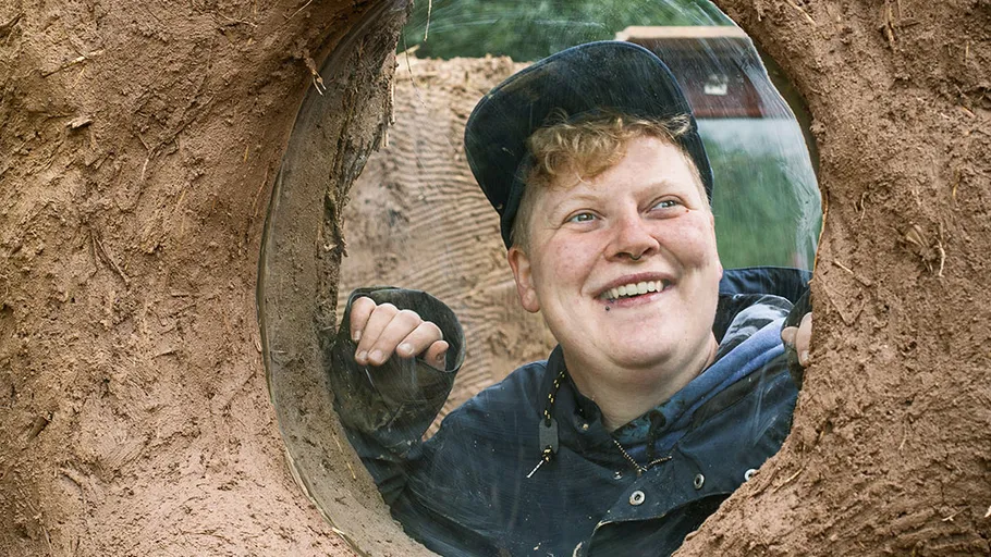 Person smiling through a circular window in a wall.