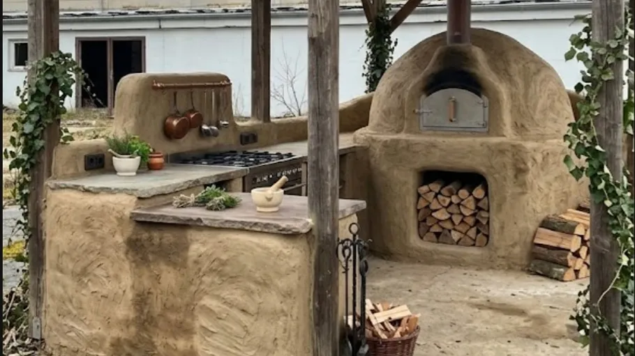 Lehmofen im Freien mit Holz, Pflanzen, Küchenwerkzeugen.