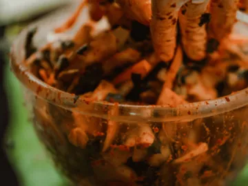One hand mixes spicy salad in a transparent bowl.