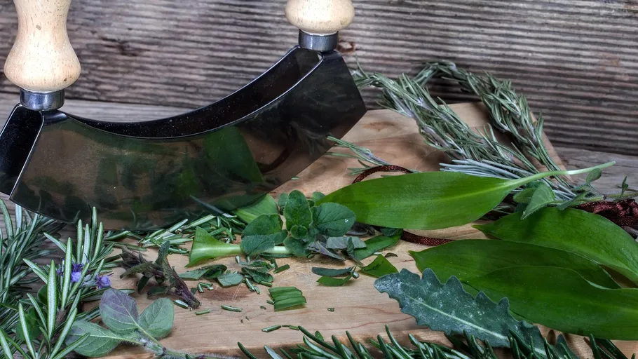 Herb chopper slicing fresh herbs on a board.