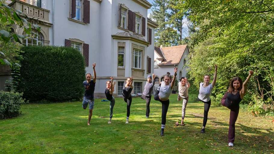 Personen machen Yoga-Posen auf Rasen.