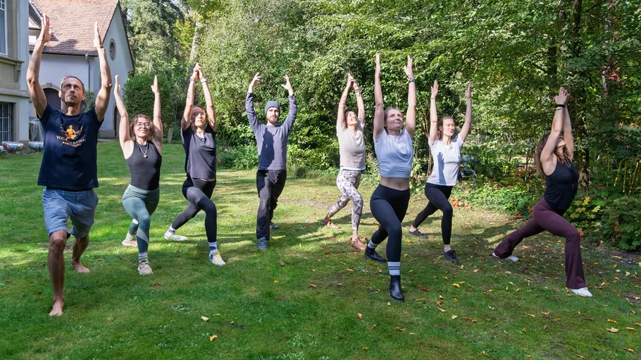 Group practicing yoga outdoors on grass.