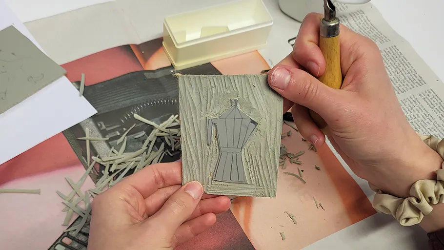 Hände schnitzen ein Kaffeekannen-Design mit Werkzeugen.