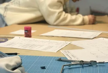 Person zeichnet mit Zeichenwerkzeugen auf Tisch.