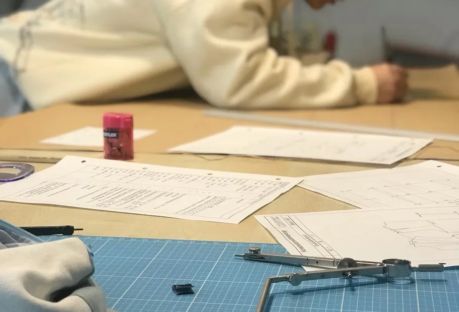 Person zeichnet mit Zeichenwerkzeugen auf Tisch.