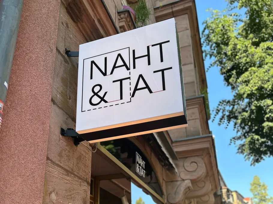 Shop sign with 'NAHT & TAT' text outside building.
