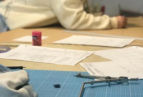 Person drawing at desk with papers and tools.