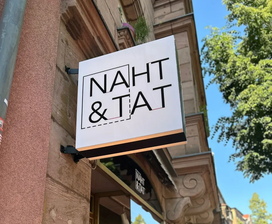 Schild mit 'NAHT & TAT' an Gebäudewand.