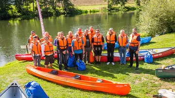 Gruppe mit Schwimmwesten steht bei Kanus.