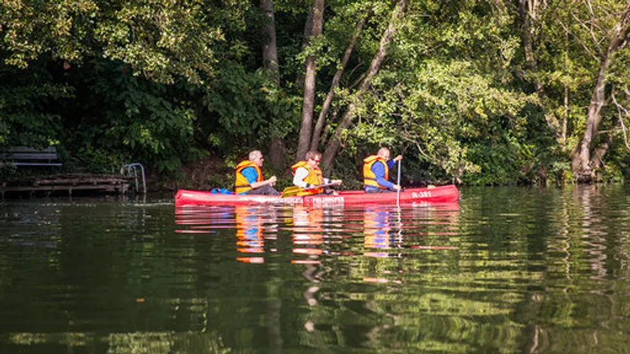 Three people canoeing on a forested lake.
