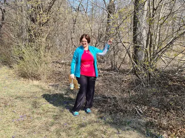 Frau mit einer Flasche in der Natur steht und lächelt.
