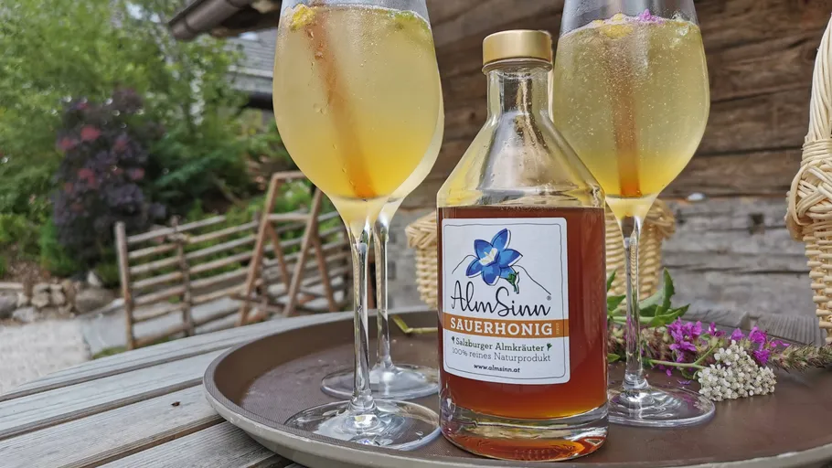 Bottle of honey with three glasses on tray outdoors.