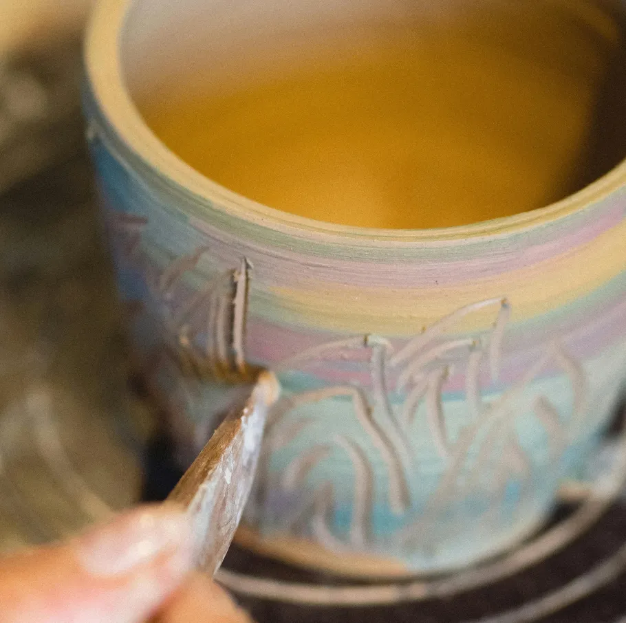 Artisan carving colorful pottery in workshop.