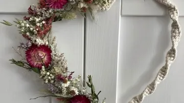 Herzförmiger Kranz mit Blumen an Tür.