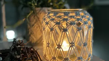 Macrame-covered candle jar on a table.