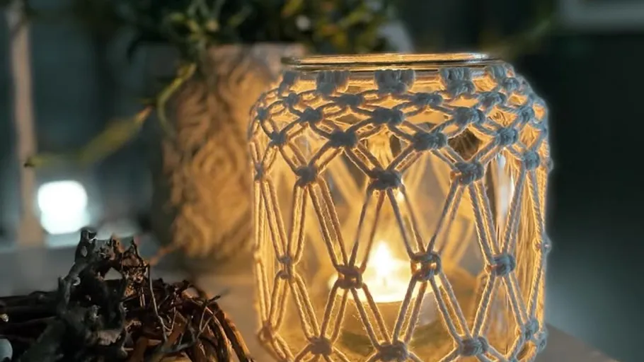 Macrame-covered candle jar on a table.