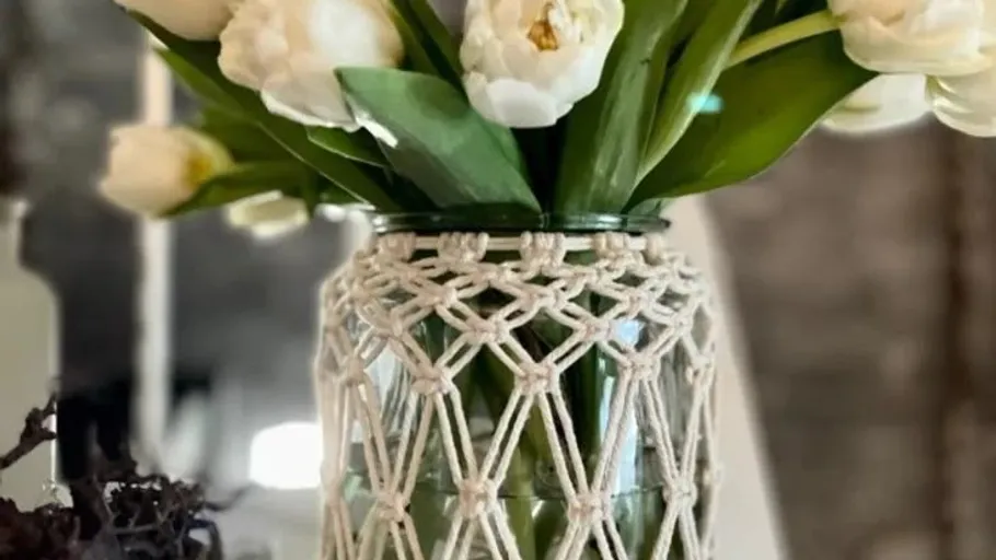 Weiße Tulpen in einer Makramee-umhüllten Vase drinnen.