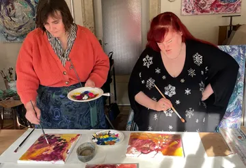 Zwei Frauen malen in einem hellen Atelier.