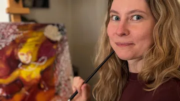 Frau hält Pinsel neben buntem Gemälde.