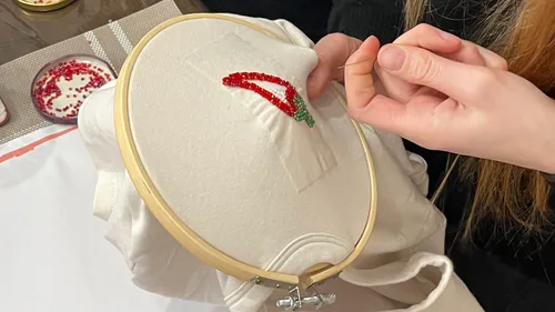 Person embroidering red chili with beads.