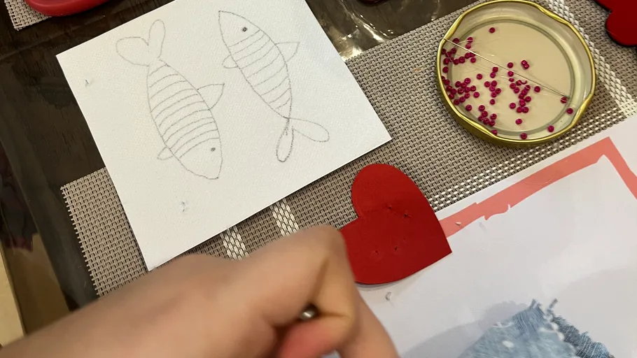 Hand nahe Fischzeichnung, Herz, Perlen auf Tisch.