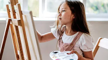 Child painting on easel indoors.