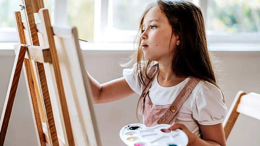 Child painting on easel indoors.