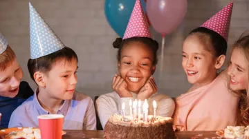 Children wearing party hats celebrate birthday cake.