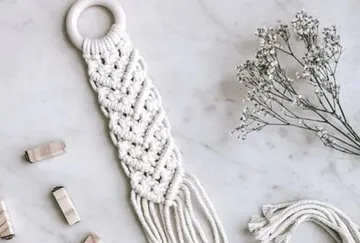 Macrame hanger hangs on table next to dried flowers.