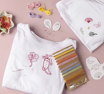 Bestickte weiße T-Shirts mit Garnen und Nadeln.