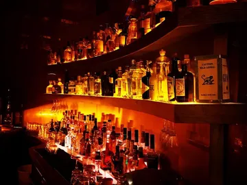 Shelves full of spirits glow in a dark room.