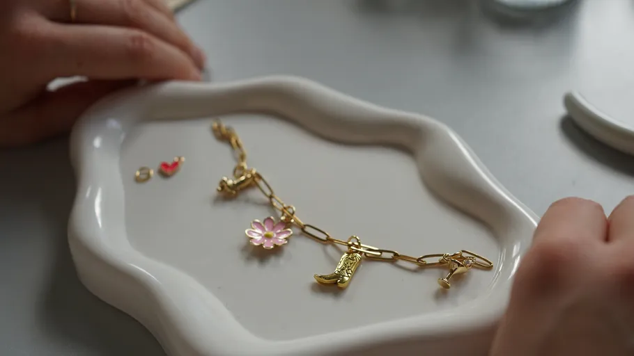 Goldenes Armband mit Anhängern auf weißer Schale.