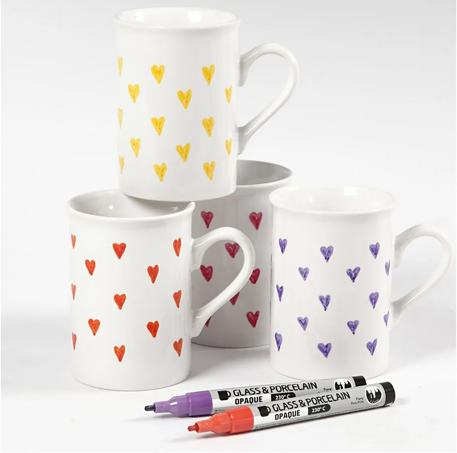 Four mugs with colorful heart patterns, markers in foreground.