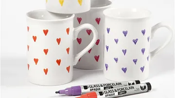 Mugs with colorful heart patterns, markers nearby.