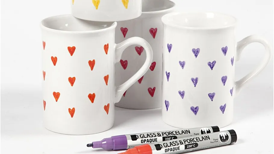 Mugs with colorful heart patterns, markers nearby.