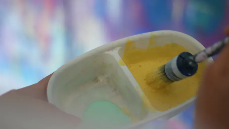 Brush mixing yellow paint in a container.