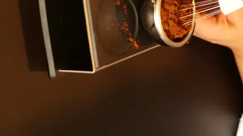 Hand mit Rührbesen und Kaffeepulver auf Tisch.