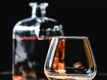 Ein Glas steht vor einer Flasche auf schwarzem Hintergrund.