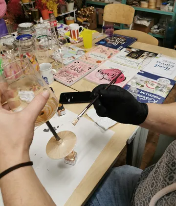 Person painting glass, surrounded by books and items.