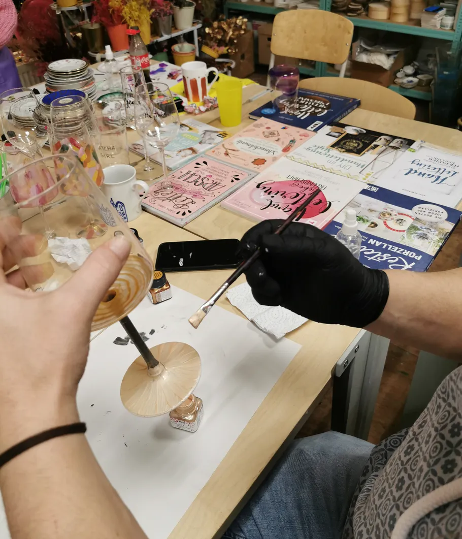 Person painting glass, surrounded by books and items.