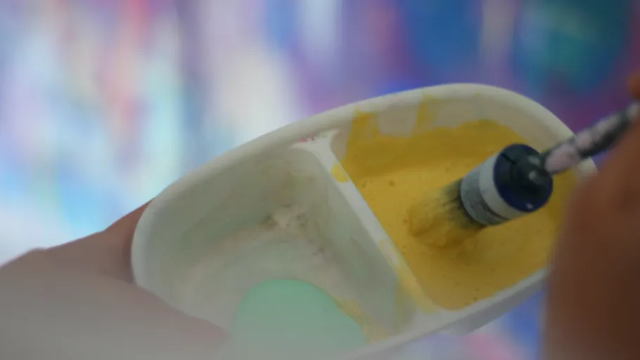Paintbrush dipped in yellow paint container.