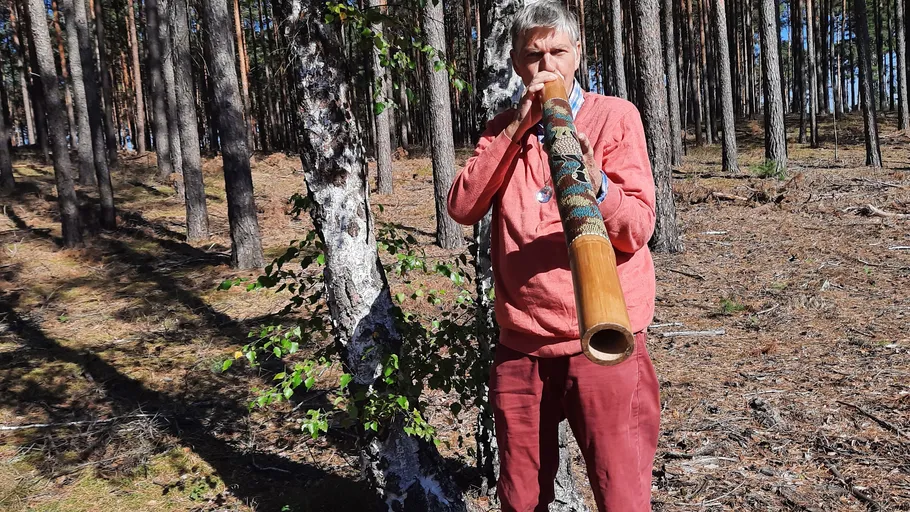 Person playing didgeridoo in a forest.