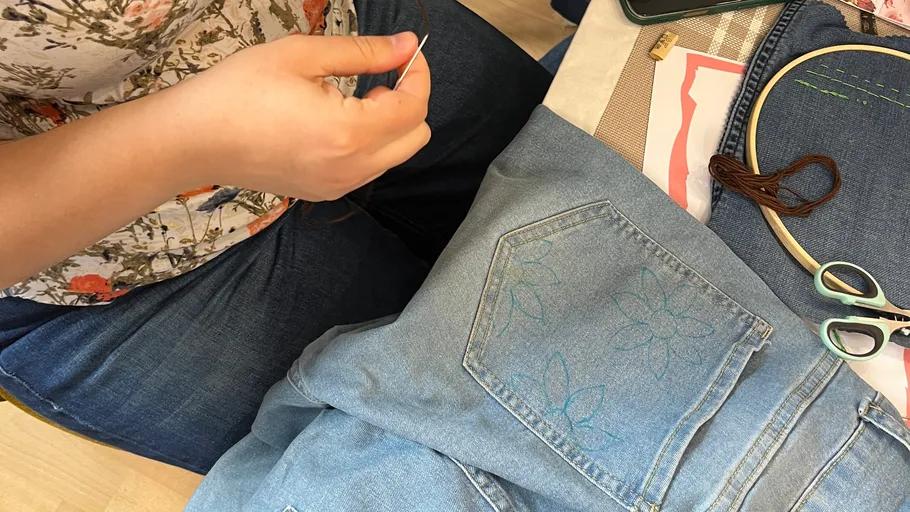 Person embroidering flowers on denim jeans.