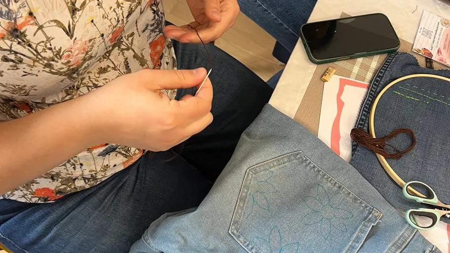 Person threading needle over denim fabric.