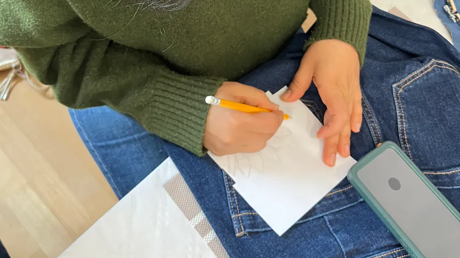 Person zeichnet auf Papier, Handy daneben.