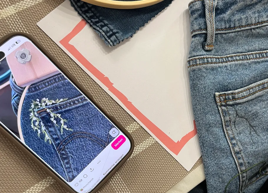 Smartphone showing jeans embroidery next to actual jeans.